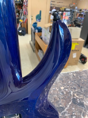 Glossy dark blue electric guitar body with subtle wave pattern, shown on a marble surface in a cluttered workshop.