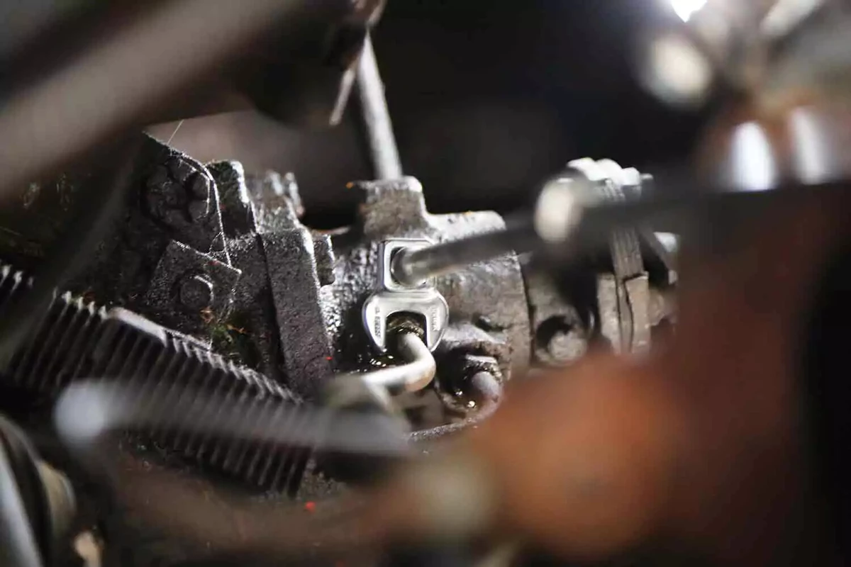A close up view of a mechanic loosening a fitting on a power-assist gearbox’s hydraulic lines with a specialized open end wrench.