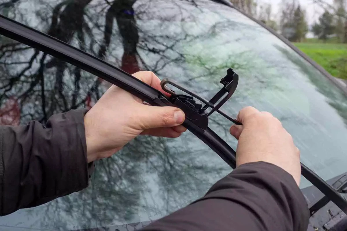 A driver wearing a winter coat replaces a windshield wiper blade.