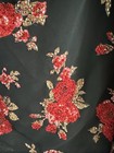 Black evening wear with red and gold floral beads and green leaves on a dark textured surface.