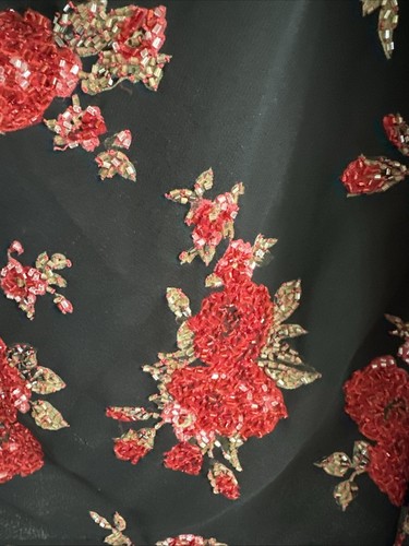Black evening wear with red and gold floral beads and green leaves on a dark textured surface.