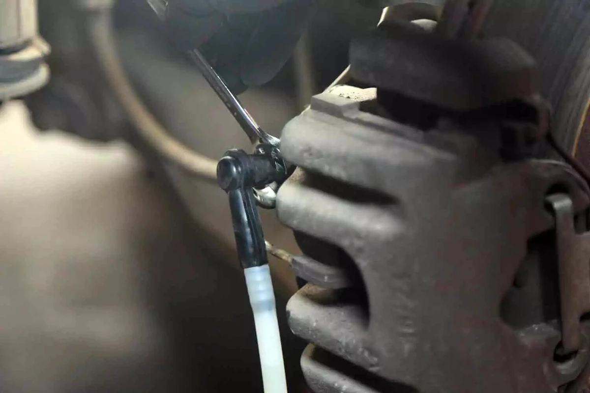 A mechanic uses a wrench to close the brake bleeder.