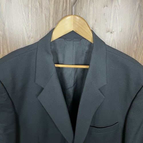 Black solid three-button blazer jacket with notch lapels, front flap pockets, and subtle textured fabric on hanger.