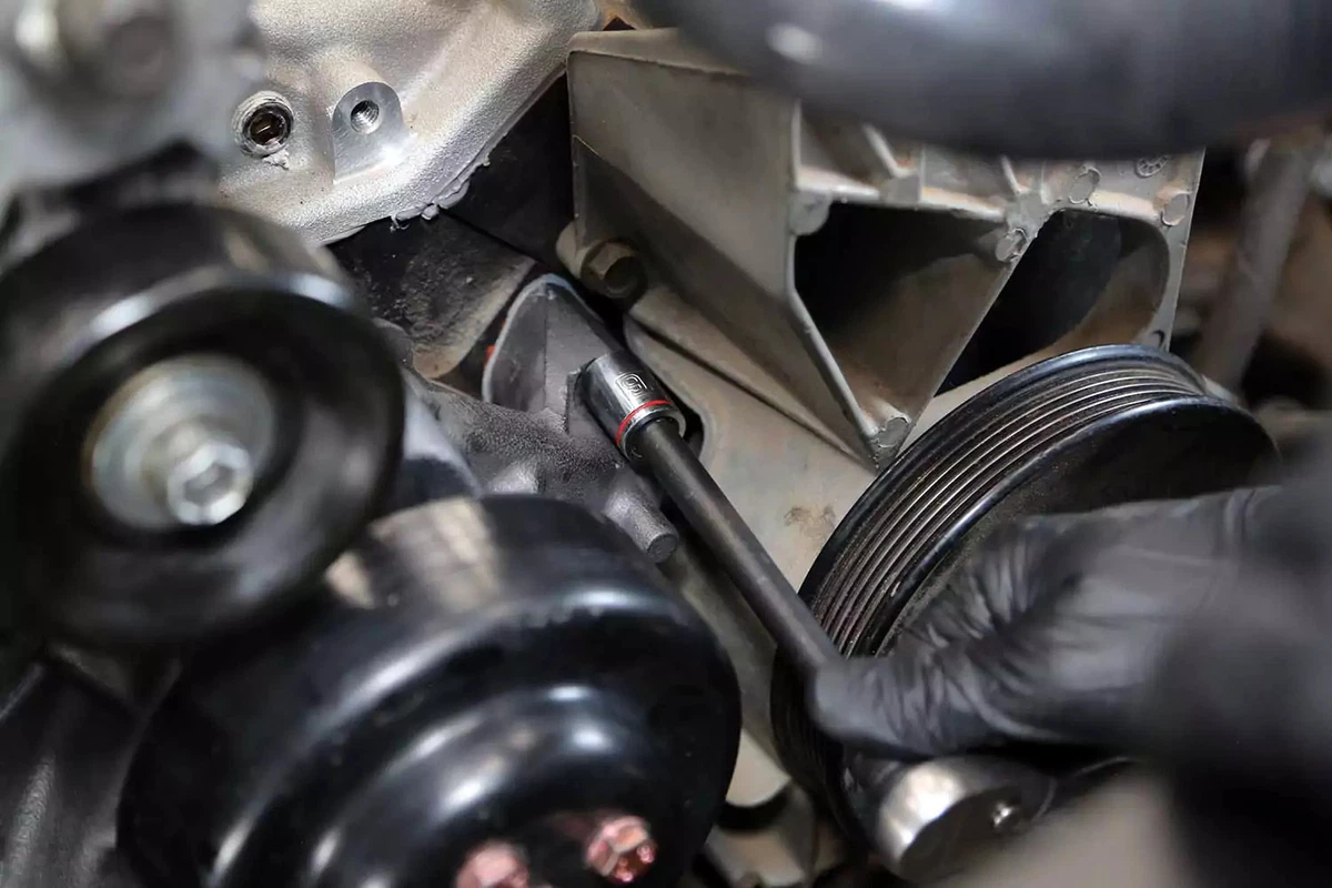 The new water pump is fastened to the engine block with a ratchet wrench.
