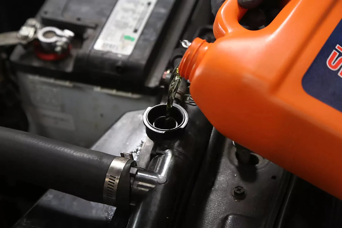 A mechanic tips a coolant jug to pour fluid into a radiator.