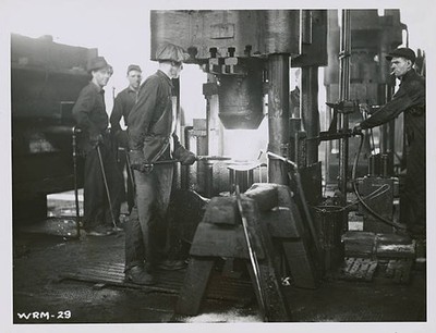 Workman places a white hot shell plank under one of giant presses - Old Photo