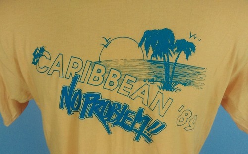 Yellow short-sleeve T-shirt with blue palm tree and beach scene graphic, text reads “Caribbean No Problem! 80’s.”