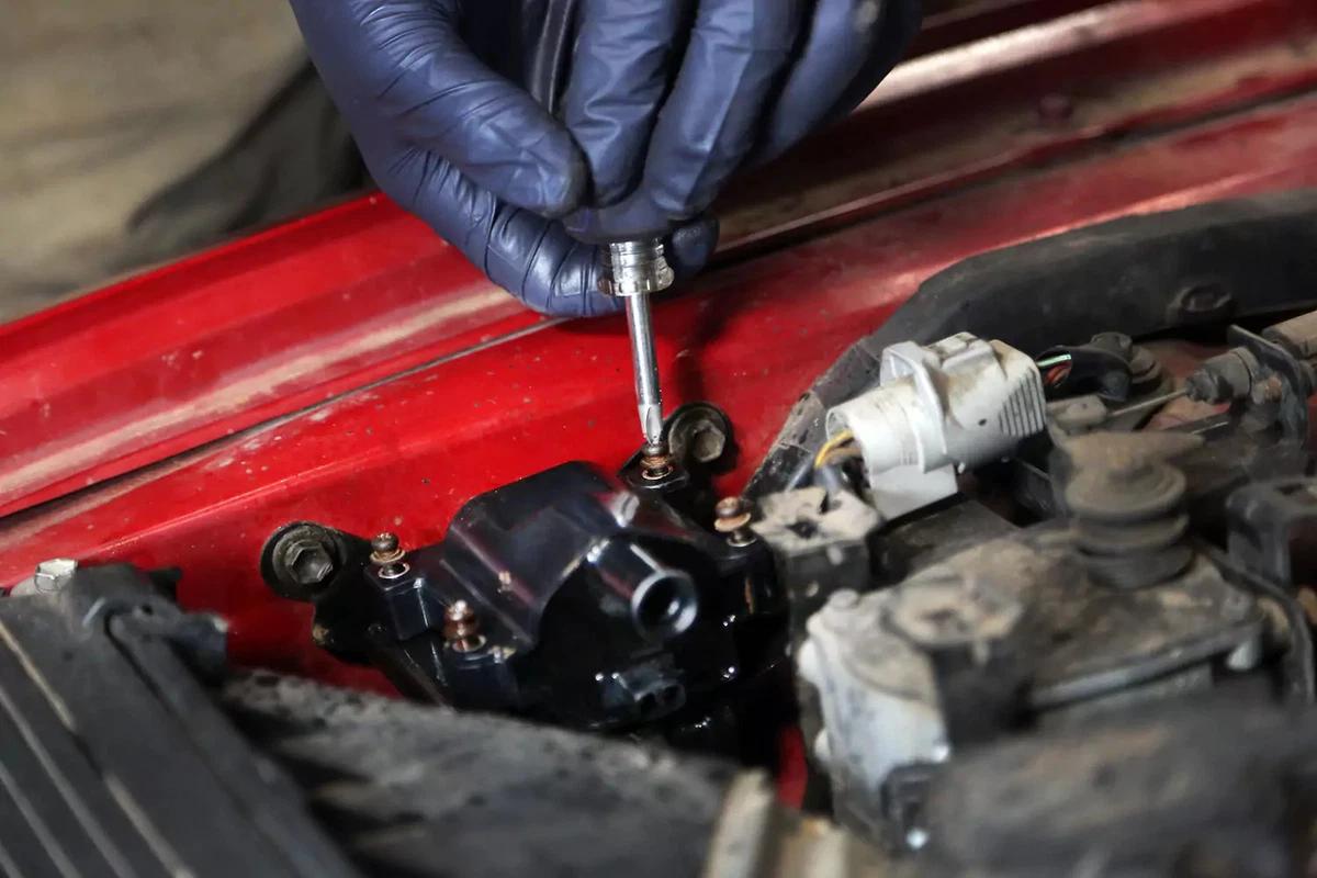 Holding a screwdriver to fasten an engine ignition coil.