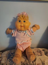 Cabbage Patch doll with pink outfit. Ribbon in hair, curly blonde hair