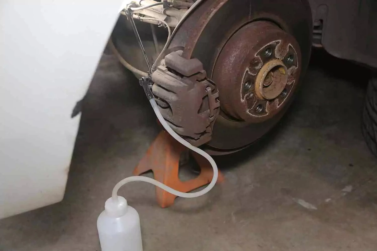 A clear drain hose extends from a vehicle's brake bleeder to a clear container on the floor.