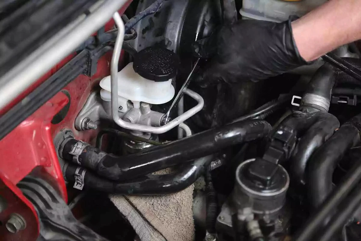 A mechanic wearing a black glove uses a line wrench to attach the fluid line to the clutch master.