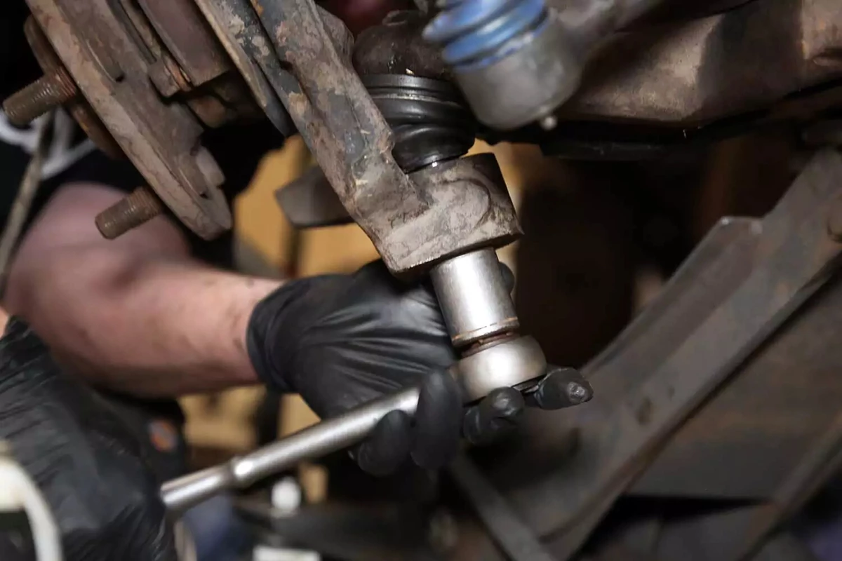 A mechanic uses a socket wrench to reinstall the steering knuckle to the new ball joint.