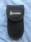 Black nylon Gerber MP600 sheath with white logo and red “USA Made” text, lying on a blue fabric background.