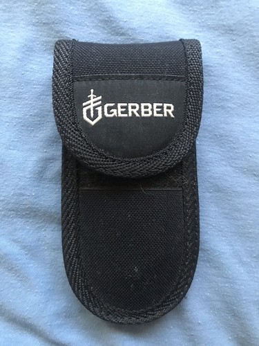 Black nylon Gerber MP600 sheath with white logo and red “USA Made” text, lying on a blue fabric background.