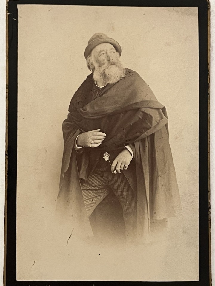 A genuinely eerie 19th-century cabinet card photo of a cloaked, flower-carrying man — the kind of one-of-a-kind antique that becomes the most-talked-about thing on any wall.