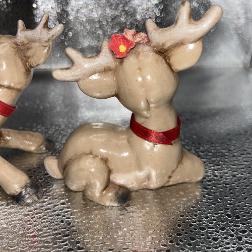 Pair of brown reindeer figurines with large antlers, red ribbons, and small red flowers on their heads.