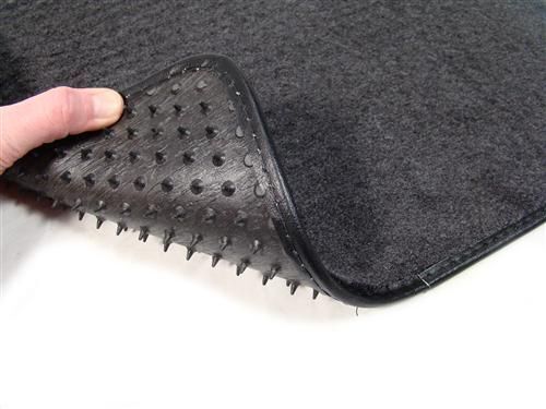 Black textured floor mat with high ridges, worn by hand on white surface.