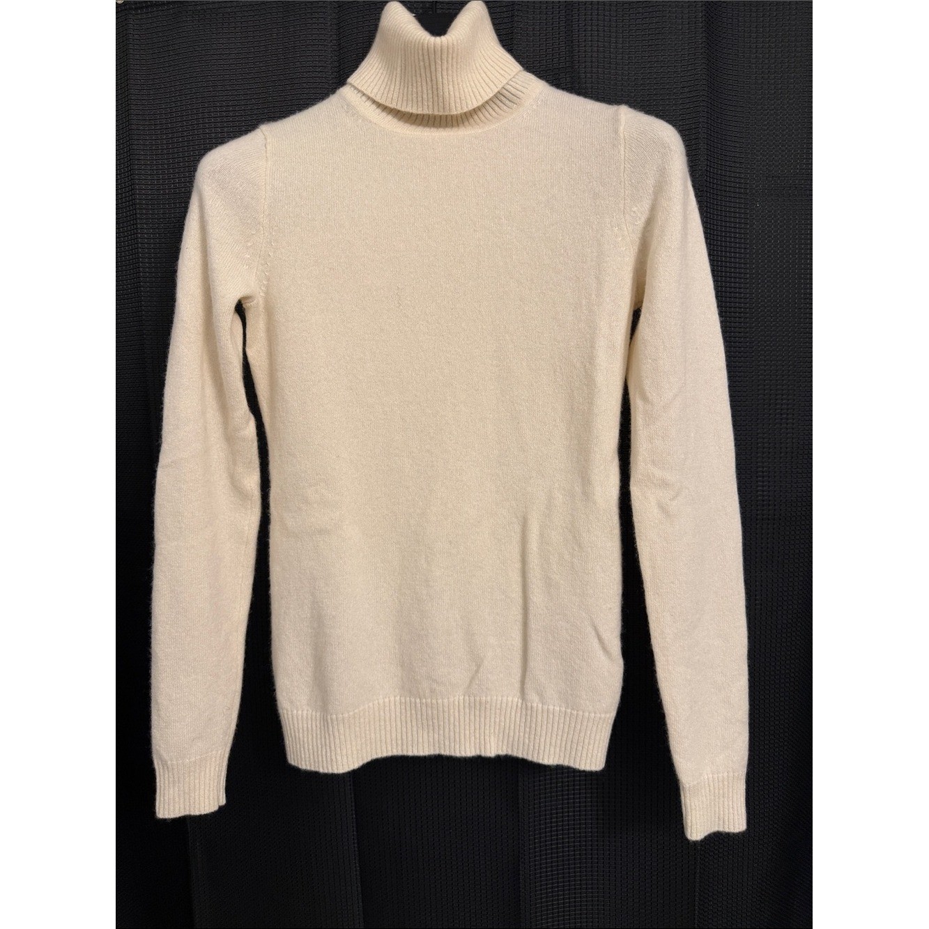 Cream cashmere turtleneck sweater on a hanger.