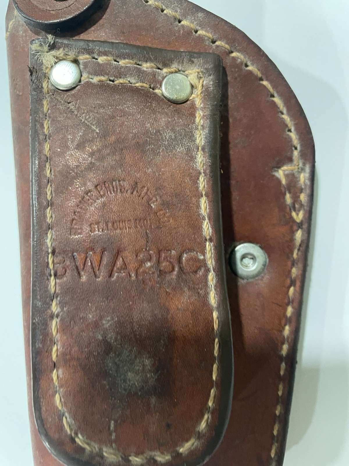 Brown leather Bauer Bros WA250 gun holster with worn white label and metal rivets, stitched on a leather panel.