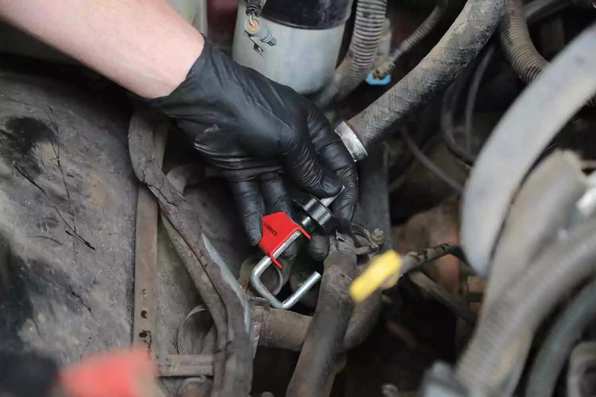 A mechanic wearing a black glove removes the clamp from a heater core hose.