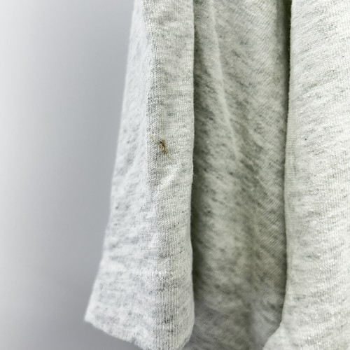 Close-up of a worn white baseball T-shirt with a small gold pinhole mark on the left sleeve, USA Made.