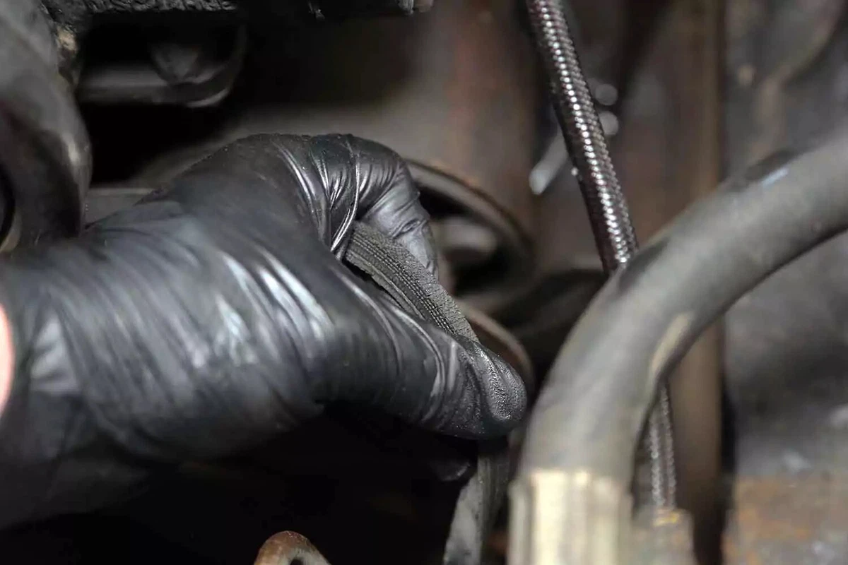 A mechanic inspects the power steering pump drive belt for fraying and weather cracks.
