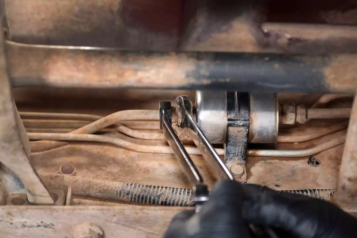 A mechanic loosens a fuel filter fitting with a line wrench and an open-end wrench.