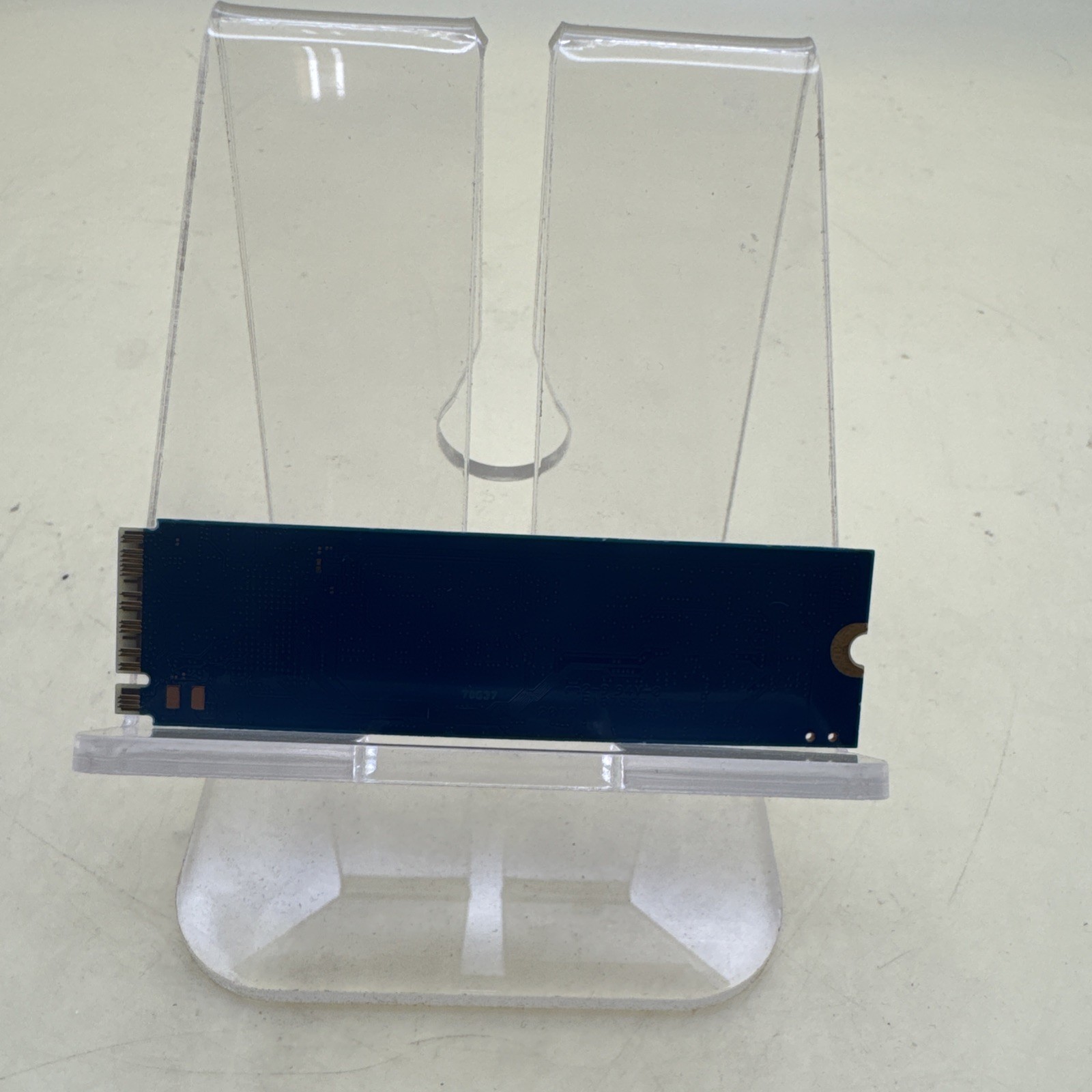 Black Kingston M.2 NVMe SSD with white text label, displayed on clear stand against plain background.