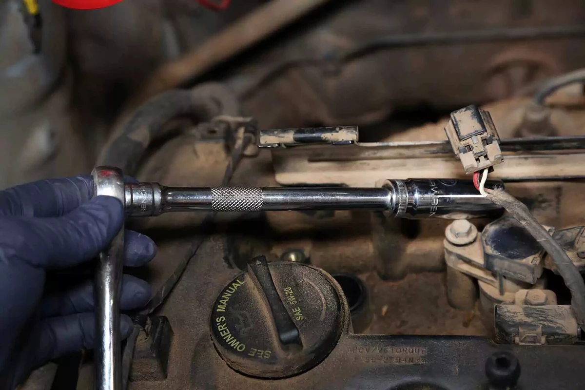A ratchet, extension, and plug socket being used to remove spark plugs.