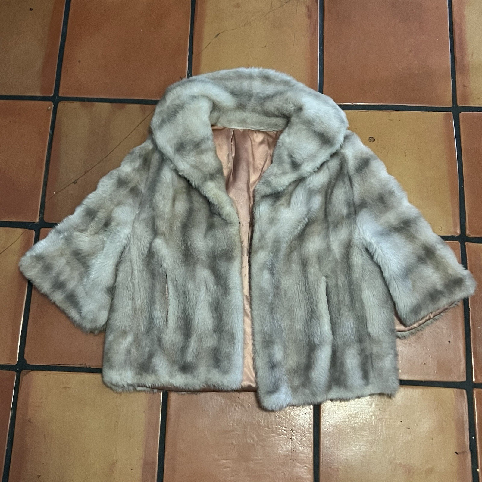 Gray and charcoal patterned faux fur cropped capelet with a rolled collar, laid flat on terracotta tile, lining partially visible.