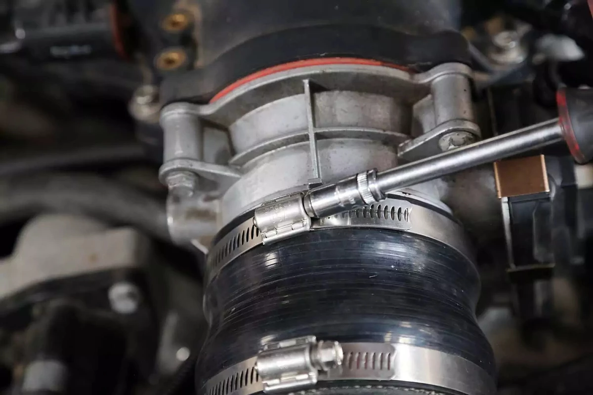 The throttle body’s hose clamp is loosened with a small socket driver.