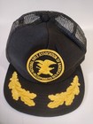 Black trucker hat with yellow National Rifle Association logo and text, featuring two yellow leaf embroidery accents.