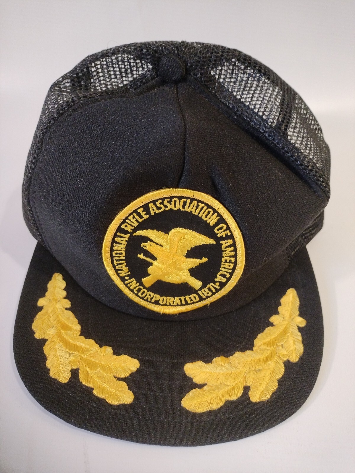 Black trucker hat with yellow National Rifle Association logo and text, featuring two yellow leaf embroidery accents.