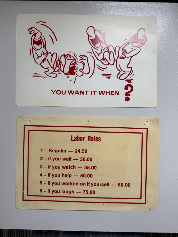 An actual 1980s garage labor-rates humor sign — the 'watching you work is extra' joke was funny then and hasn't aged a day.