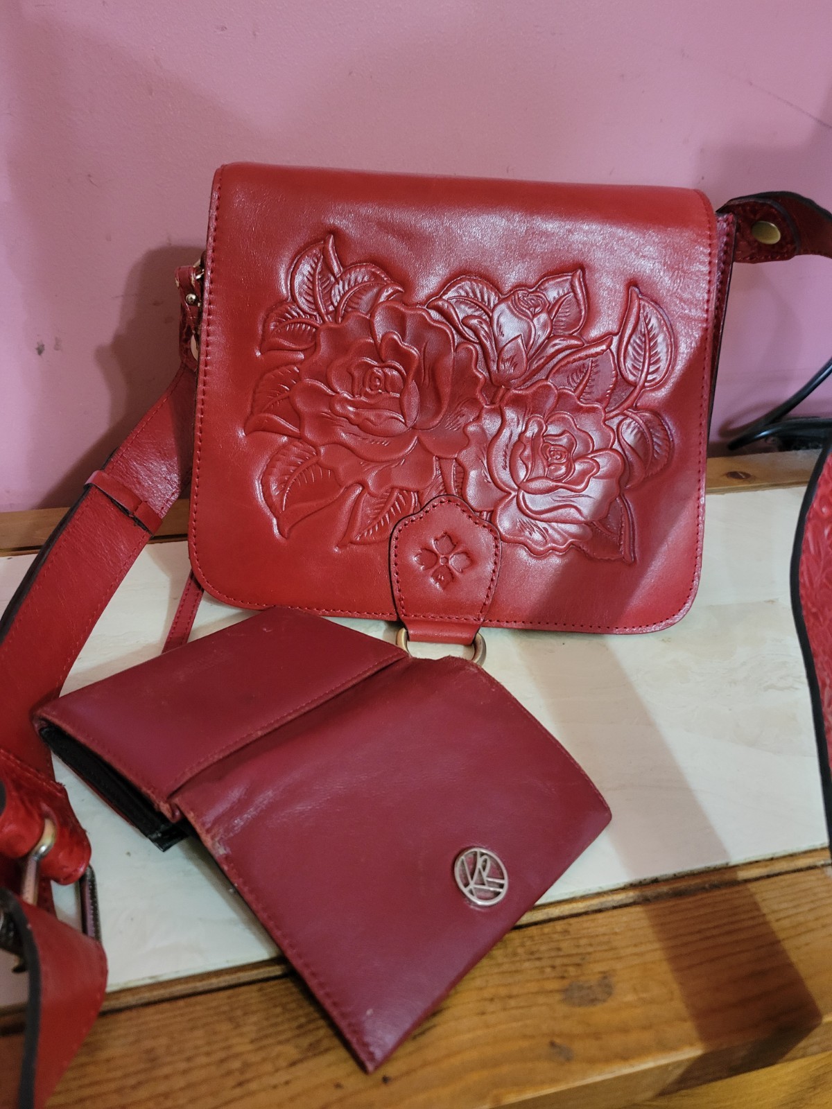 Red leather crossbody bag with an embossed rose design on the flap, shown with a matching wallet.