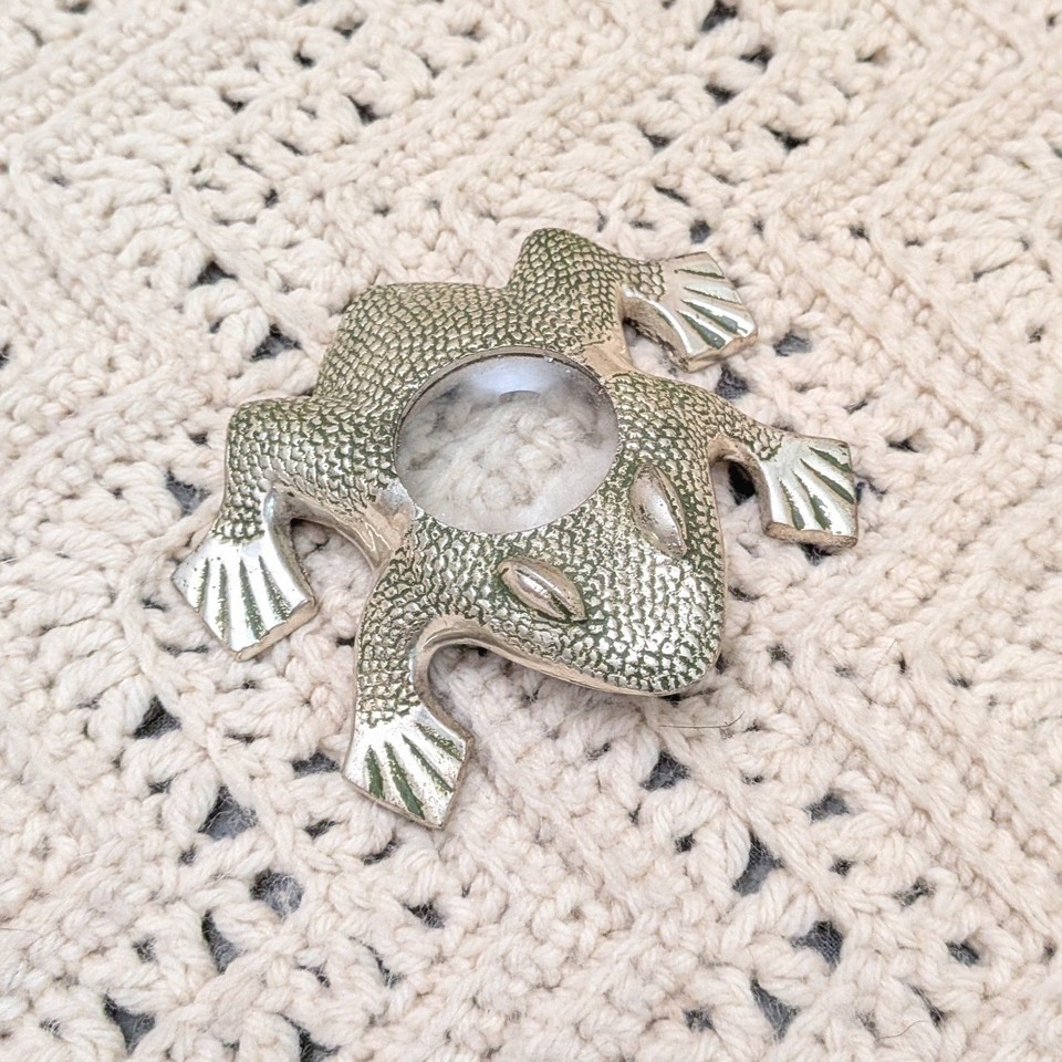 A silver-tone frog clutching a magnifying glass — part paperweight, part desk sculpture, all whimsy.
