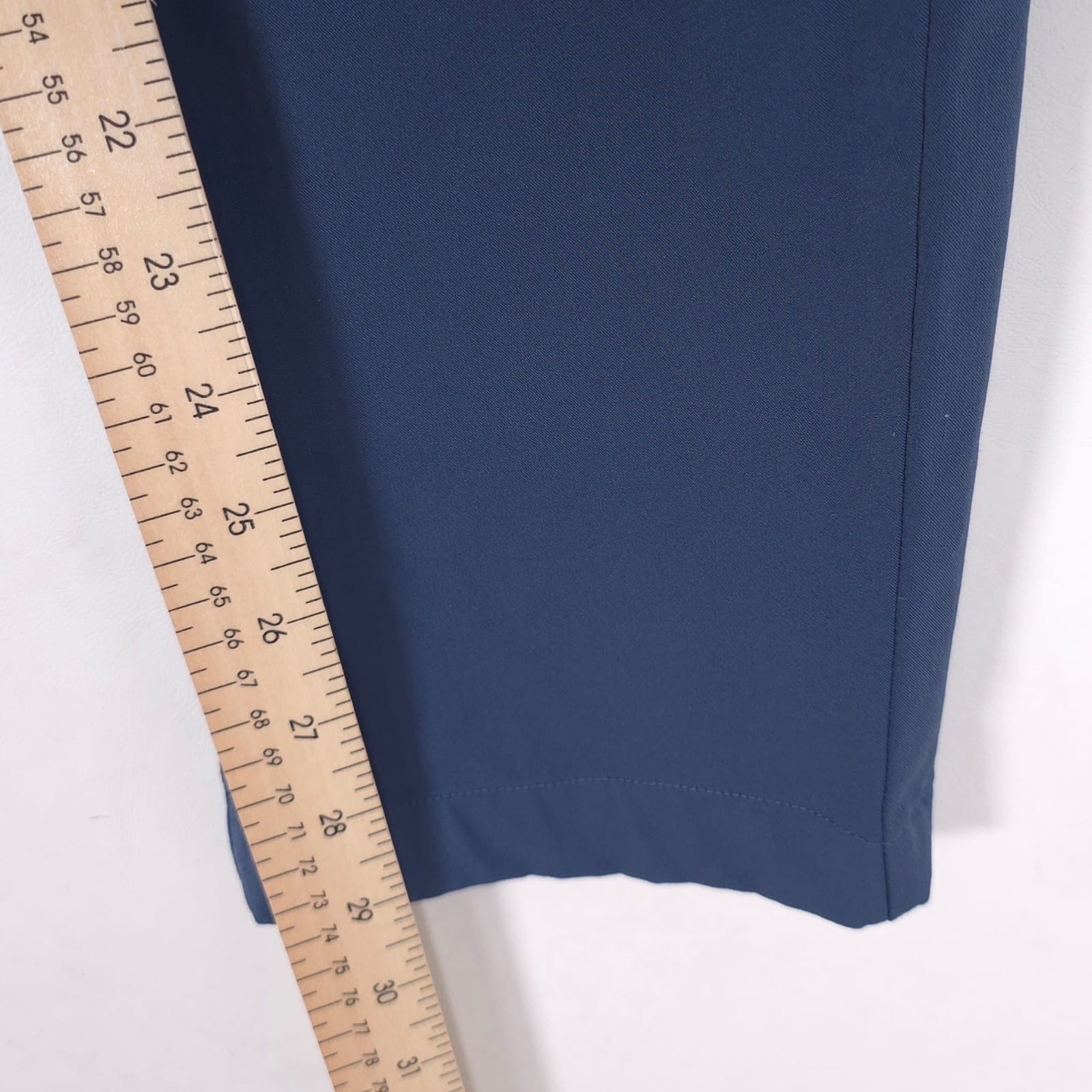 Measuring blue Theory men’s dress pants at 32 slim fit with dark vertical seam, using yellow ruler with black markings.