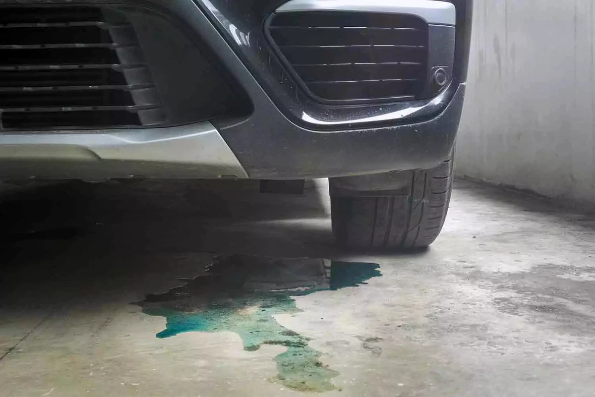 A blue-green puddle of engine coolant on the concrete underneath the front of a car.