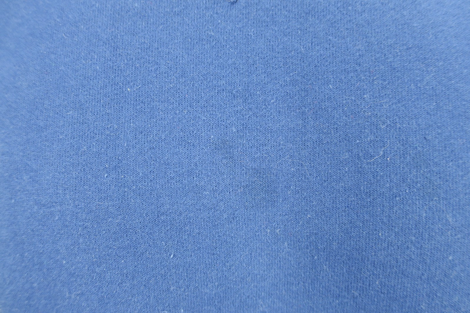 Solid blue VTG 90s Russell Athletic sweatshirt fabric with small white fiber flecks on a textured light gray surface.