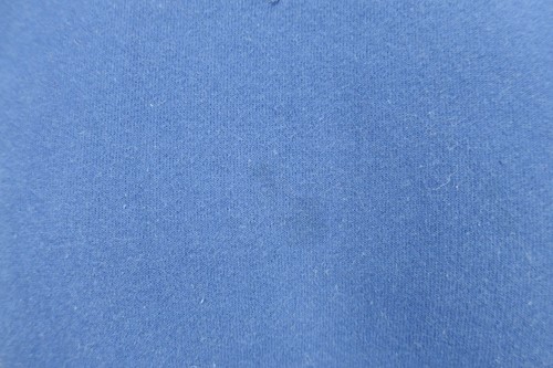 Solid blue VTG 90s Russell Athletic sweatshirt fabric with small white fiber flecks on a textured light gray surface.