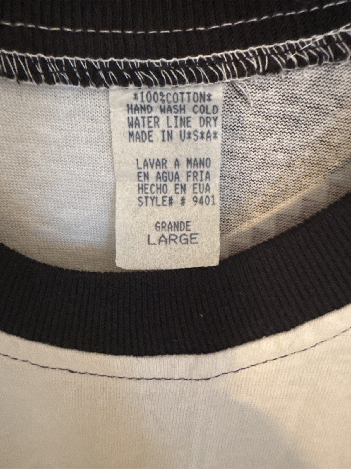 White vintage T-shirt with black trim, size large, featuring a sewn neck label reading “100% Cotton Hand Wash Dry Made in U.S.A.”