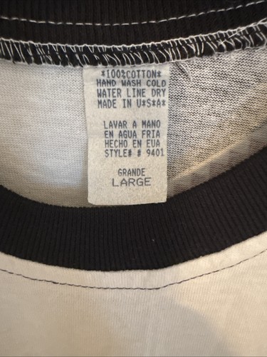 White vintage T-shirt with black trim, size large, featuring a sewn neck label reading “100% Cotton Hand Wash Dry Made in U.S.A.”