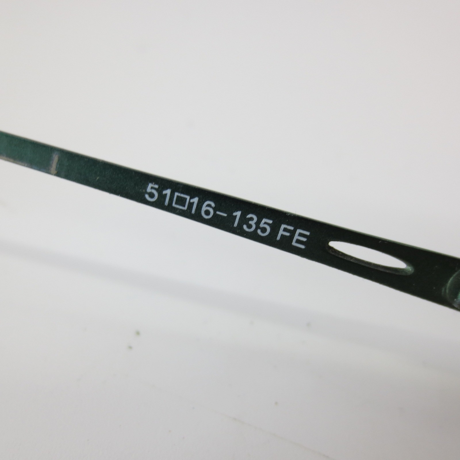 Green metal semi rimless oval eyeglass frames with white printed text reading “51016–135 FE” and a cutout lens tab.