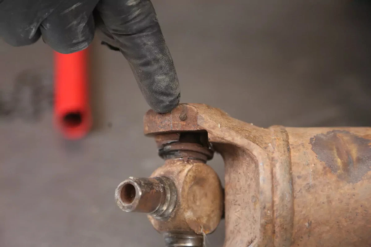 A mechanic wearing a black glove points to the driveshaft's thermoplastic retainers.