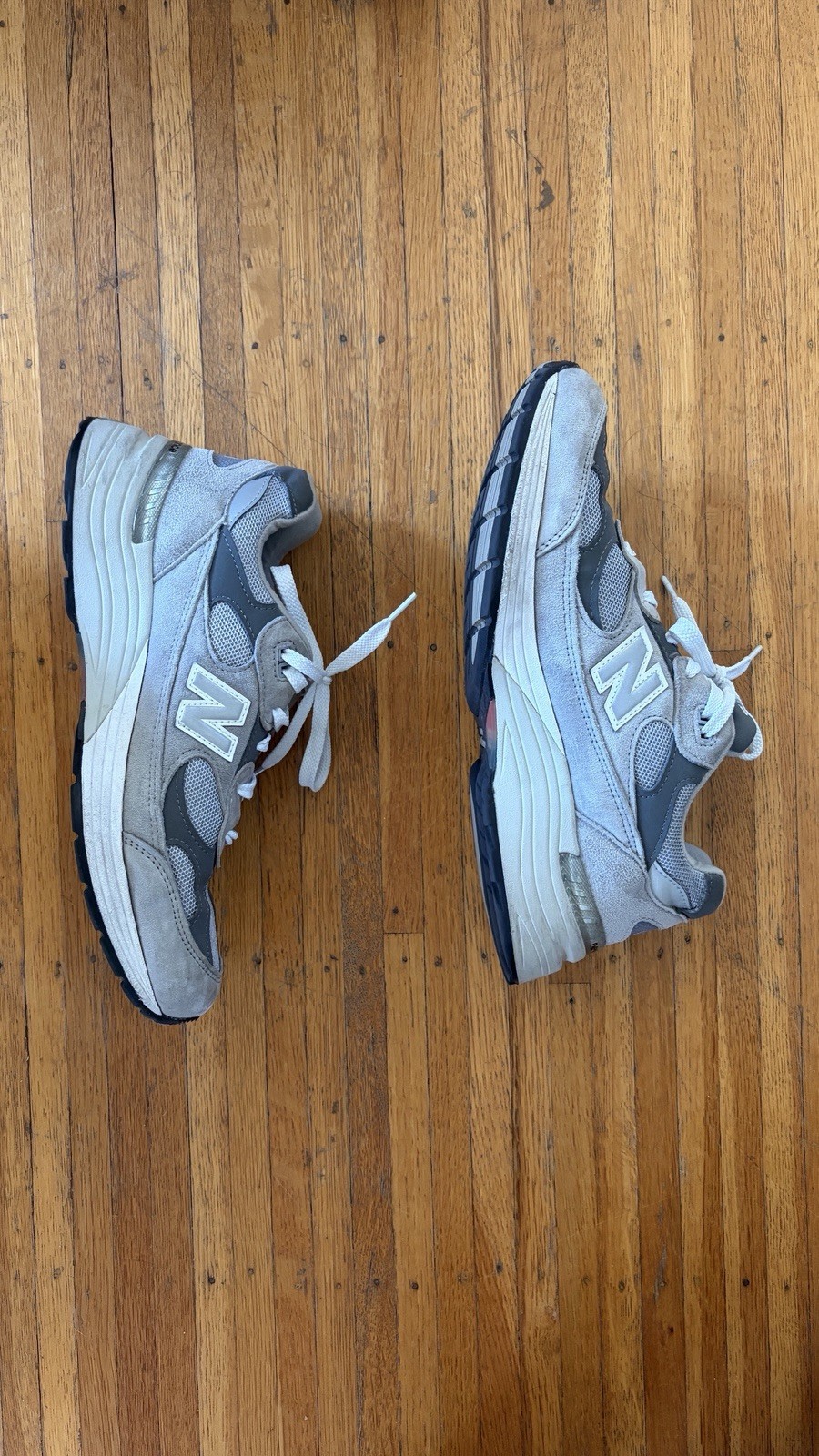 Grey New Balance 992 mens size 9 with silver “N” logo, white midsoles, and blue accents on wooden floor.
