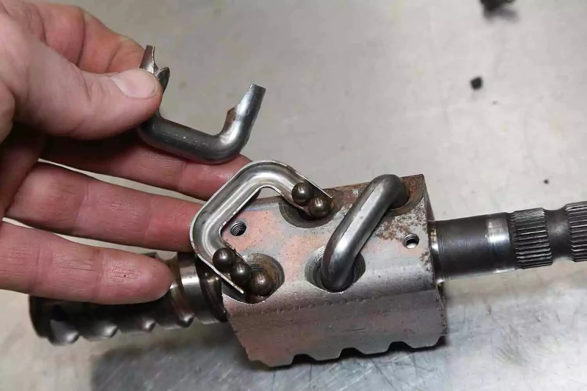 A mechanic displays a vintage steering system worm gear’s open loop, revealing five recirculating ball bearings.