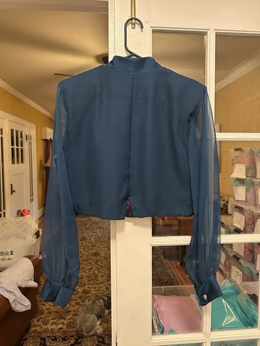 Teal long-sleeve J.R. Nites by Caliendo blouse with mock neck, displayed on hanger against white door.