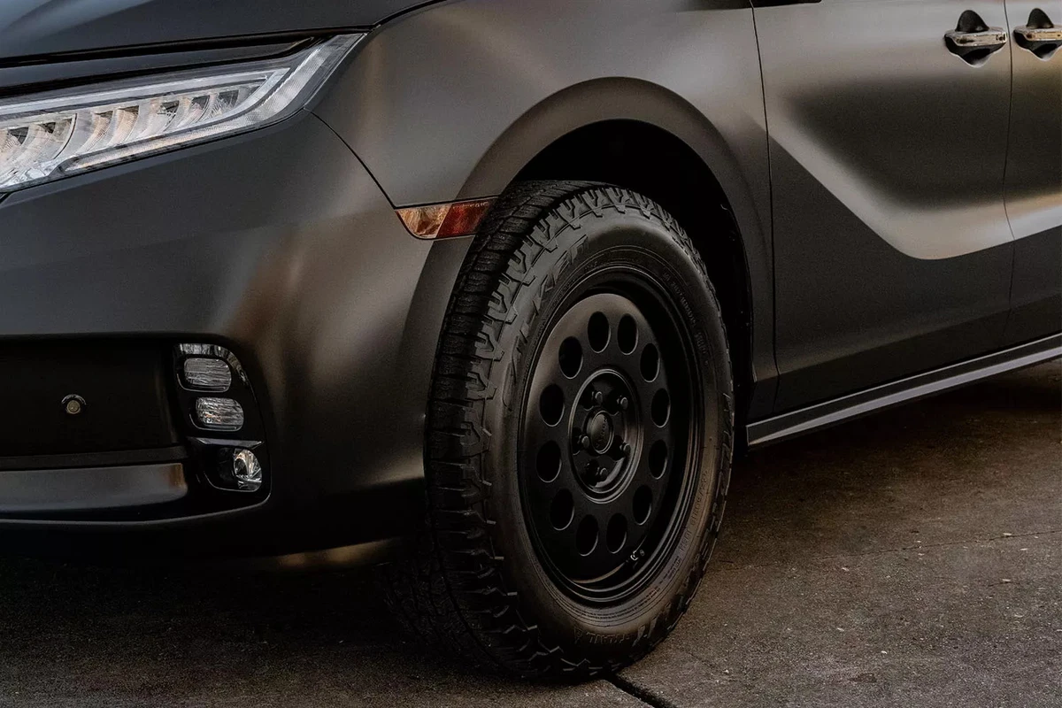 The front left wheel and tire of a modified minivan.