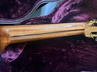 Brown wood fretboard with white diagonal stripe, gold hardware, and subtle “Laviolette” branding on dark purple plush.
