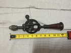 Vintage black and red hand crank drill with worn wooden storage handle, yellow tape measure, and visible branding.